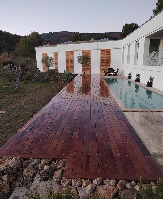 Terrasse en bois luxe et piscine moderne en couloir de nage Longue terrasse en bois exotique menant à un couloir de nage rectangulaire devant une maison blanche moderne aux volets à lattes.