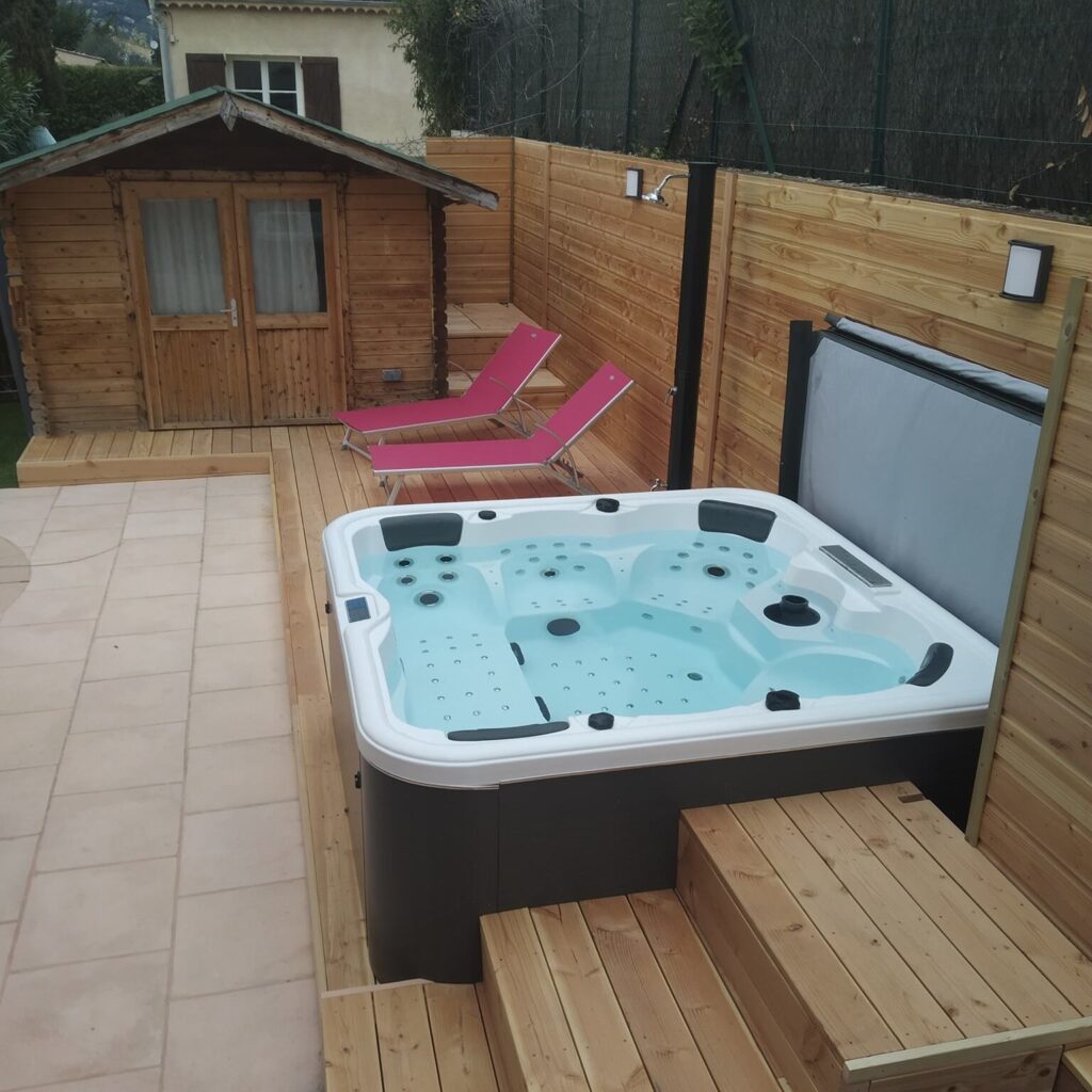 Aménagement extérieur avec spa et terrasse en bois Spa de luxe et transats roses sur terrasse boisée à côté d'un cabanon de jardin. Espace détente extérieur moderne.